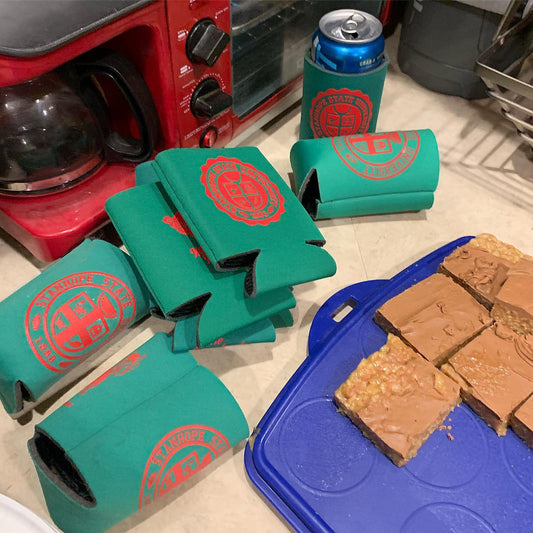 Green can coolers with red logo on a counter next to brownies and a blue container.