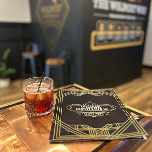 Glass of a red cocktail with a straw on a coaster next to a 'Wildcat Distilling Co. Tasting Room' menu.