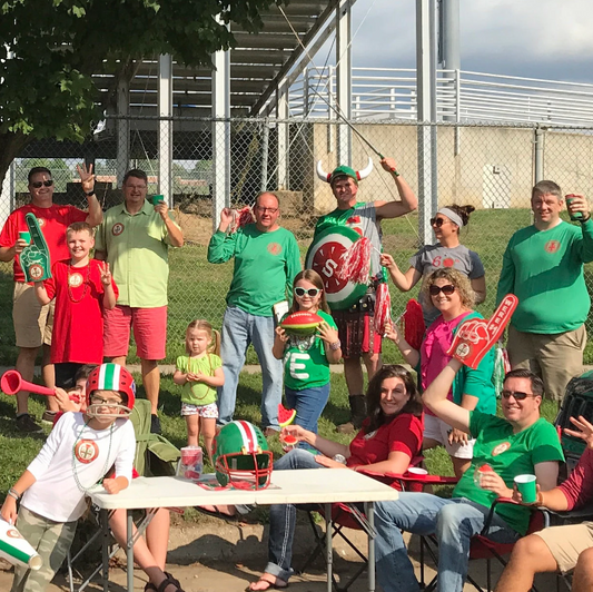 Group of people in green and red attire with sports equipment, possibly fans or supporters, outdoors.