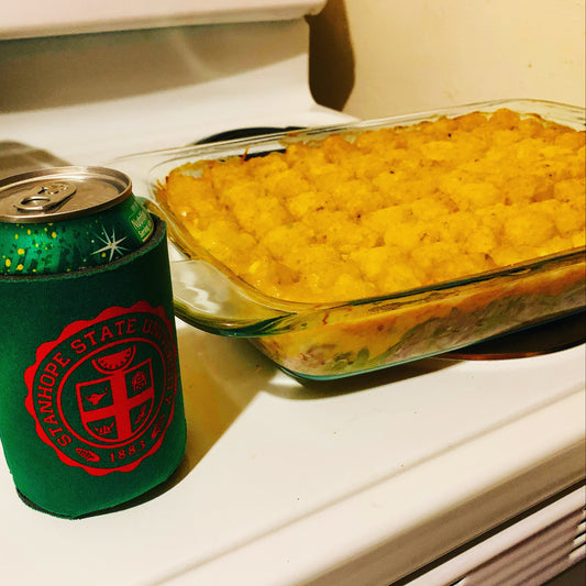 Glass dish with a casserole next to a green can cooler on a stove.